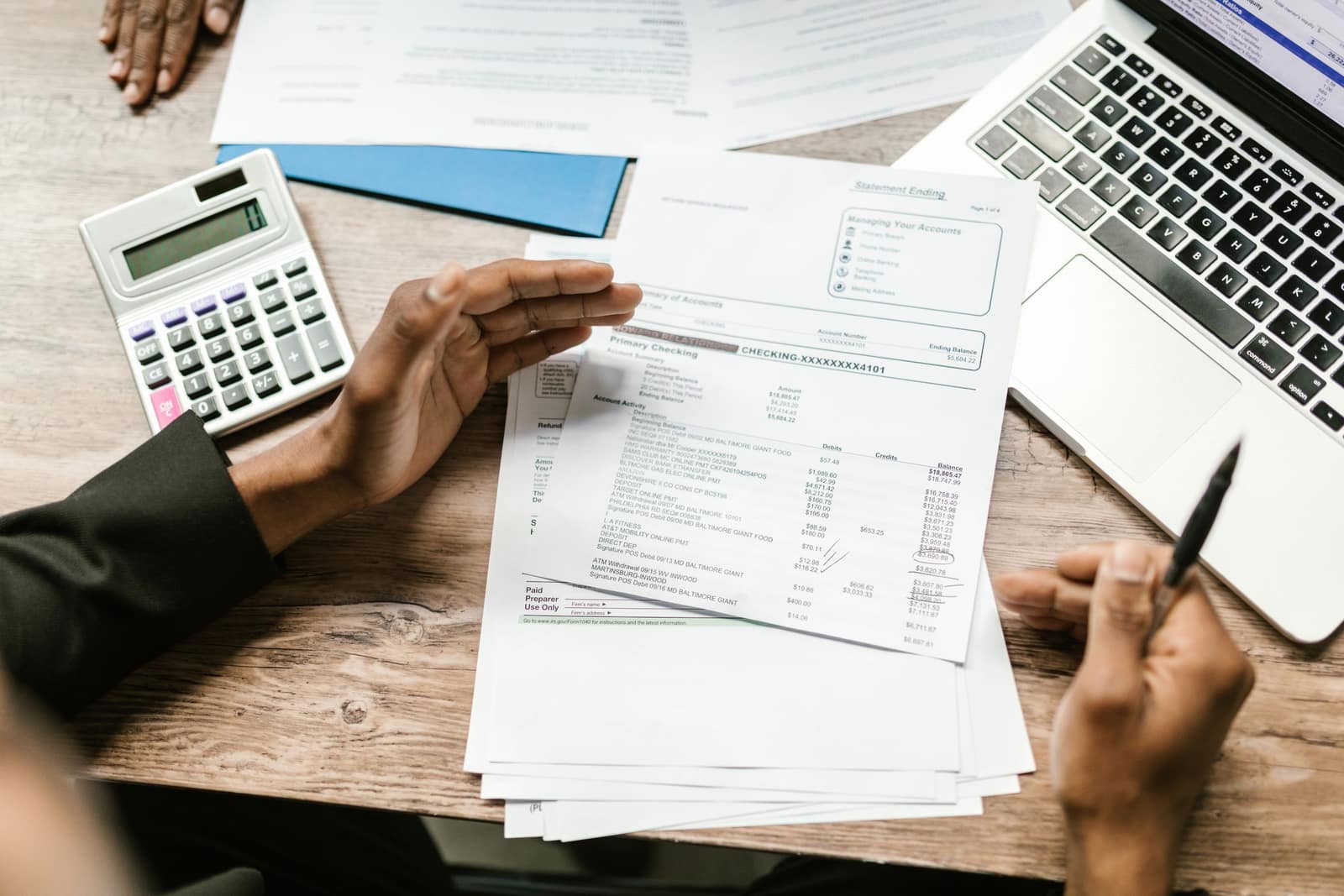 Hands reviewing account statements beside a calculator and a laptop