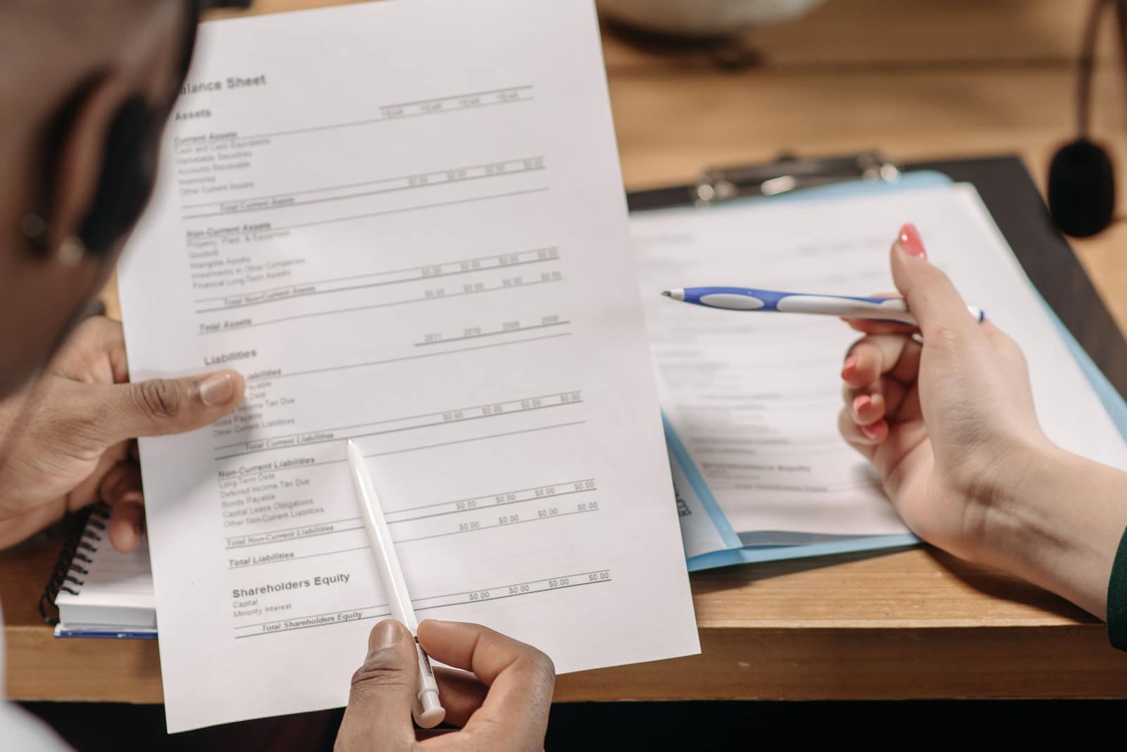 Two people reviewing a printed balance sheet and notes at a desk