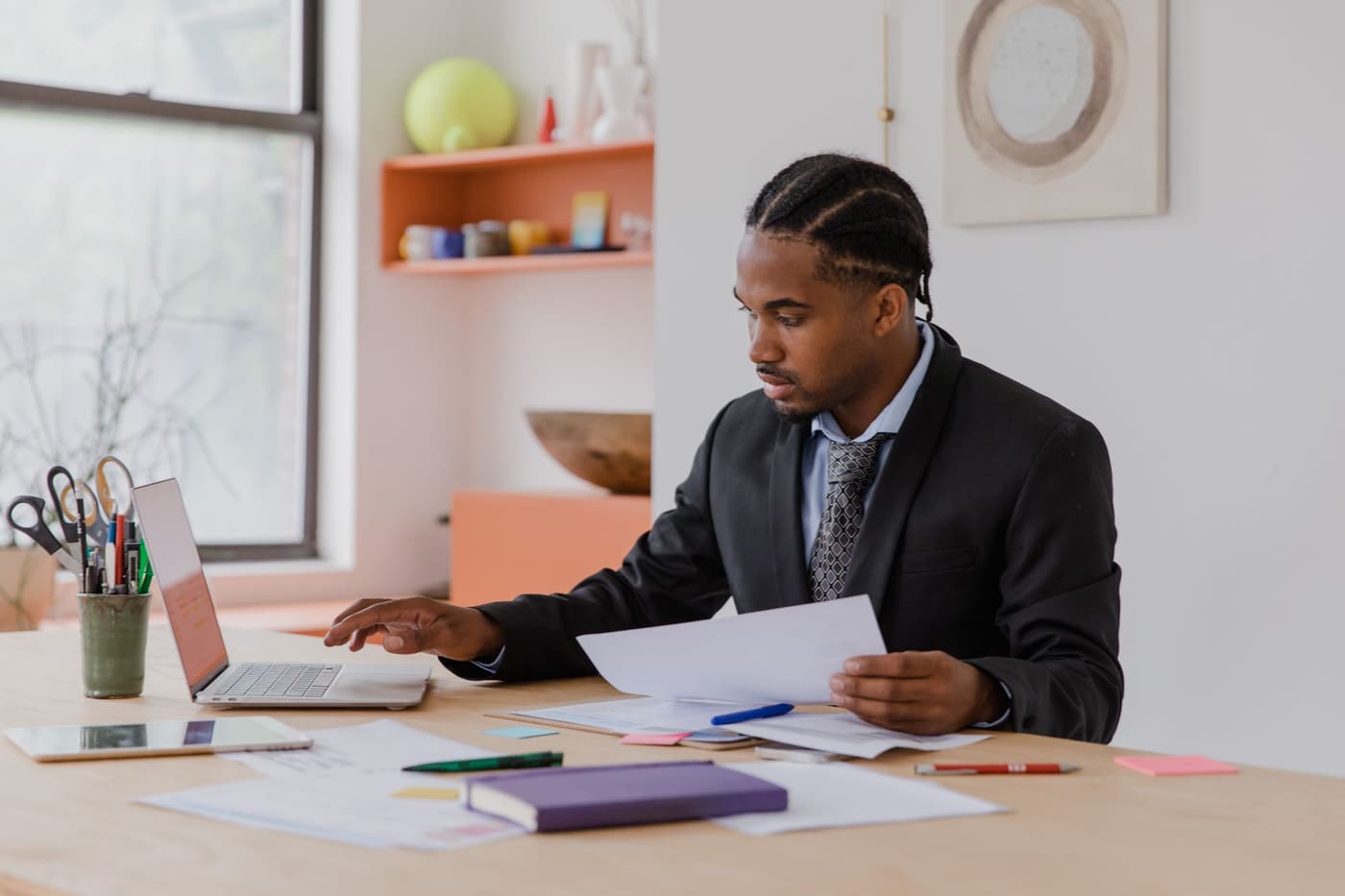 Professional reviewing papers at a desk while working on a laptop